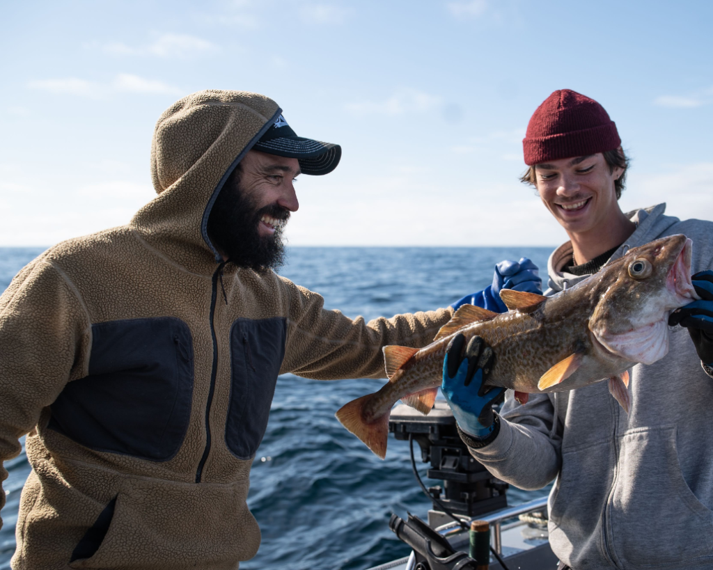 Captain Grayson standing next to a guest holidng a cod during a ketchikan fishing charter.