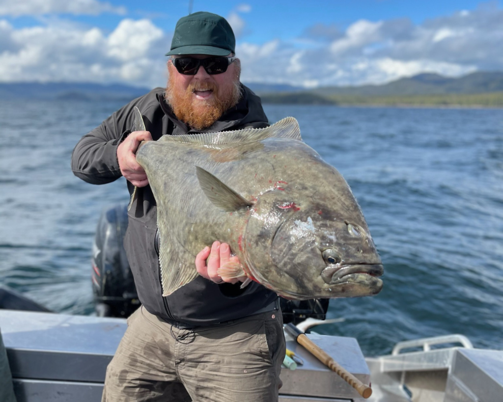 Captain Jake holding a huge pacific halibut on a boat during a ketchikan fishing charter.