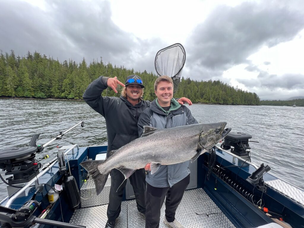 Captain Lukas standing next to a guest holding a massive king salmon.