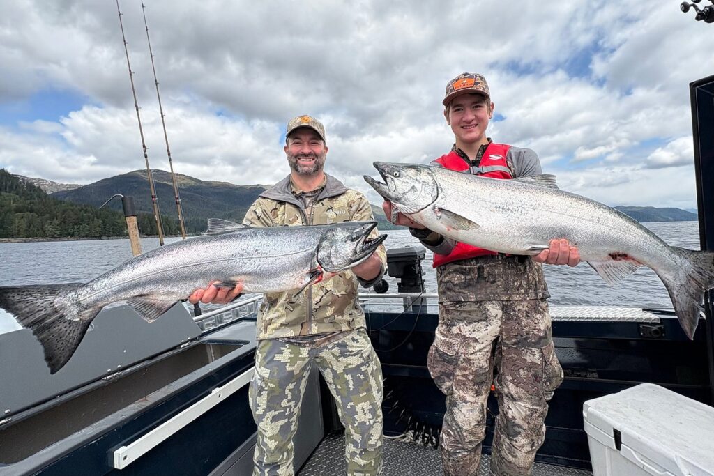 Two men holding massive salmon on a cloudy day during a fishing charter.
