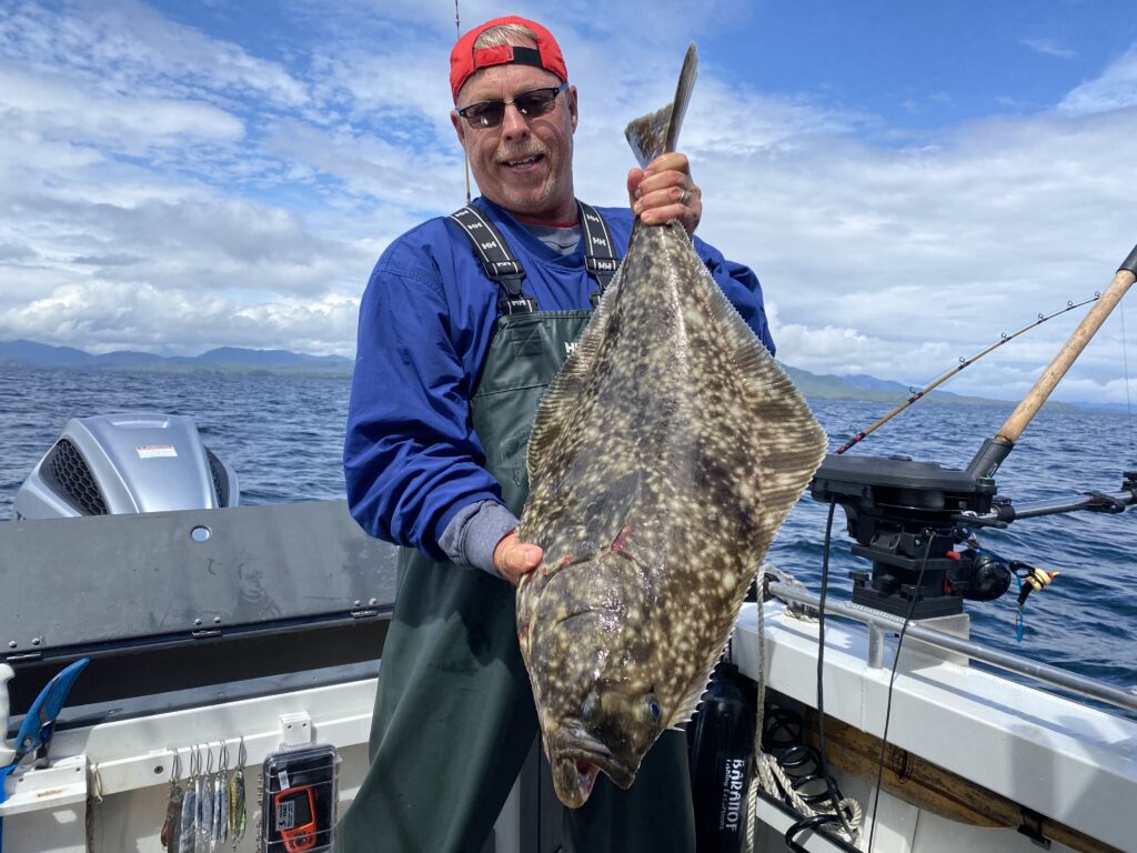 A man holding a massive halibut on a sunny day standing on a boat.