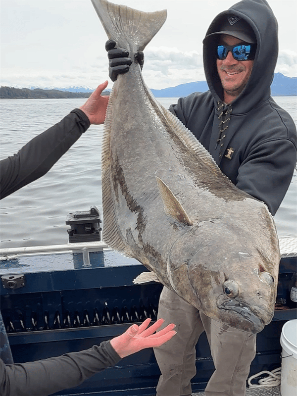 Captain Lukas of Ketchikan's Finest Fishing Charters holding a massive halibut on a cloudy day